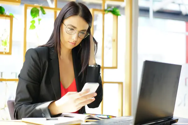 Kameraya gülümseyen dizüstü bilgisayarlı, modern ofiste çalışan gözlüklü mutlu esmer iş kadını. Başarılı Girişimcilik ve Kariyer Konsepti.                            