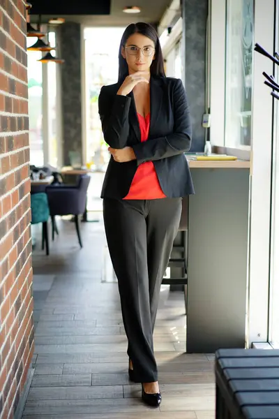 Siyah takım elbiseli şık bir beyaz iş kadını elinde bir cep telefonu ve tabletle elinde müşterilerin iletişime geçmesini bekliyor..