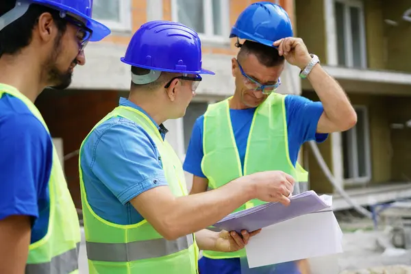 Three construction workers discussing blueprints at building site outdoors