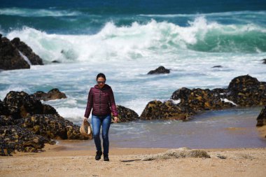 Genç bir kadın Portekiz, Porto 'da kumlu ve mavi gökyüzü olan boş bir kumsalın keyfini çıkarıyor..