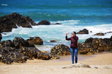 Genç bir kadın Portekiz, Porto 'da kumlu ve mavi gökyüzü olan boş bir kumsalın keyfini çıkarıyor..