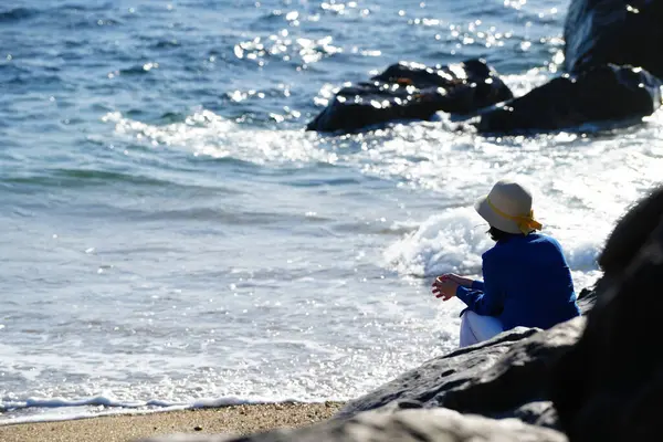 Genç bir kadın sahildeki bir kayanın üzerinde oturuyor..