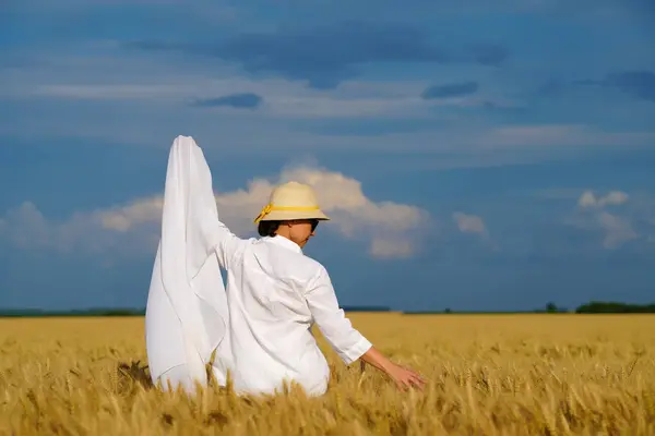 Altın buğday tarlasında beyaz elbiseli güzel bir kadın hasada hayran..