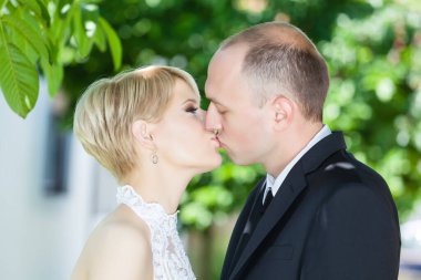 Romantik çift güneşli düğün gününde dışarıda öpüşüyor.