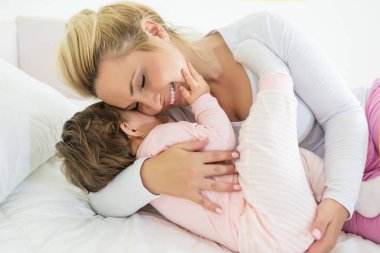 Gülümseyen bir kadın, küçük bir çocuğu kucaklarken, evde yan yana yatıyor.