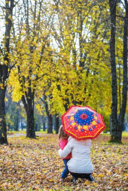 Anne ve kızı sonbahar parkında şemsiye altında.