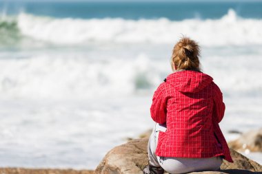 Yalnız bir kadın kayanın üzerinde oturmuş okyanusa bakıyor. Tanımlanamayan biri.