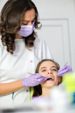 Kadın dişçi, dişçi aletleri kullanan genç bir kadını muayene ediyor.