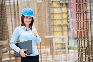 İnşaat alanında elinde dizüstü bilgisayarla gülümseyen kadın.
