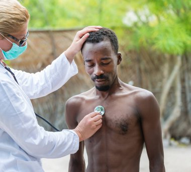 Doktor steteskop kullanarak üstsüz adamı muayene ediyor.