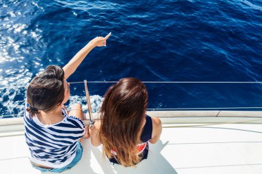 Mavi sulara bakan güvertede yan yana oturan iki kişi.