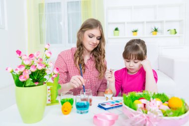Anne ve kızı evin içinde renkli paskalya yumurtaları boyuyor.