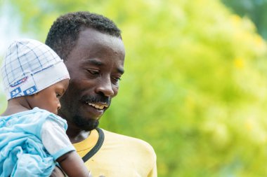 Güneşli bir günde bebeği kucağında tutan gülümseyen bir adam.