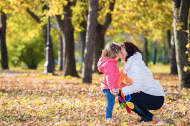 Anne, sonbahar ağaçlarının arasında diz çöküp kızını kucaklıyor.