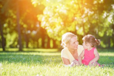Gülümseyen kadın güneşli çimenlerde genç kızın yanında yatıyor.