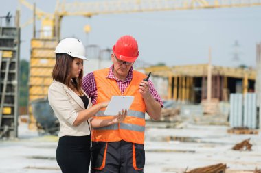 Kadın mühendis dışarıda erkek inşaat işçisiyle proje detaylarını tartışıyor.