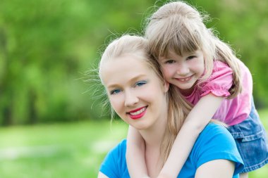 Gülümseyen kadın, güler yüzlü kızı bahar günü dışarı taşıyor.