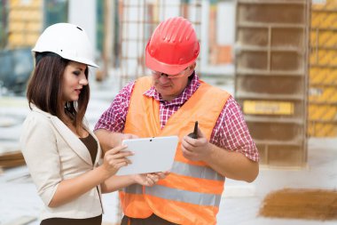 Erkek işçiyle inşaat planlarını tartışan kadın mühendis.
