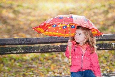 Sonbahar öğleden sonrasında elinde renkli şemsiyeyle oturan genç kız