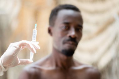 Aşı sırasında doktorun elinde üstsüz bir adamın yanında şırınga vardı.