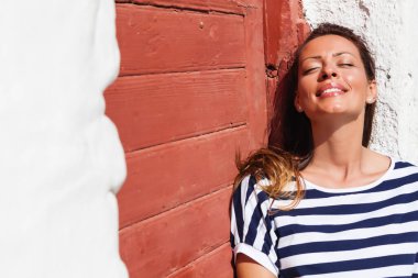 Genç, mutlu kadın ahşap kapının önünde oturuyor, gülümsüyor, düşünüyor..