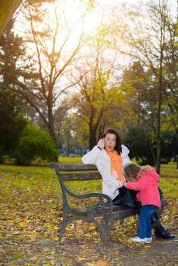 Annesi telefonda, küçük kızı annesinin çantasına bakarken.