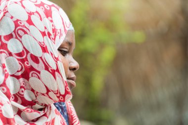 Kafasında fular olan Afrikalı siyahi bir kadının yan resmi..