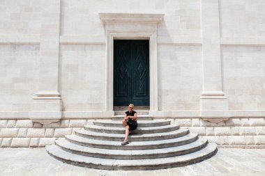 Hırvatistan 'ın Dubrovnik kentindeki giriş merdivenlerinde oturan motosiklet kasklı gülümseyen kadın