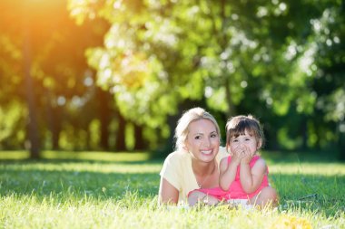 Anne ve küçük kızı ön tarafta uzanıp parktaki kameralara bakıyorlar.