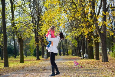 Anne küçük kızını havada tutuyor. Sonbahar Parkı