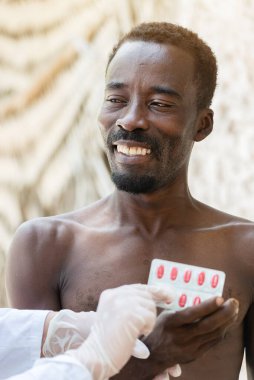 Gülümseyen Afrikalı siyahi adam doktordan ilaç alıyor.