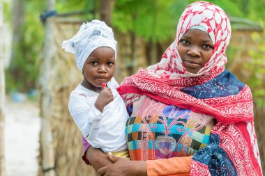 Afrikalı siyahi kadın küçük kızı kucağında tutuyor ve kameraya bakıyor.