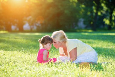 Anne gün batımı parkında küçük kızıyla konuşuyor, çimlerin üzerinde yatıyor.