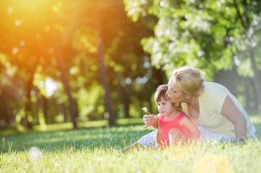 Anne gün batımı parkında küçük kızıyla konuşuyor, çimlerin üzerinde yatıyor.