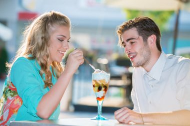 Gülümseyen genç çift açık kafede meyve salatası yiyor. 