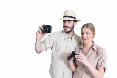 Safari kıyafetli heyecanlı bir çift fotoğraf çekiyor ve beyaz arka planda dürbün tutuyor.