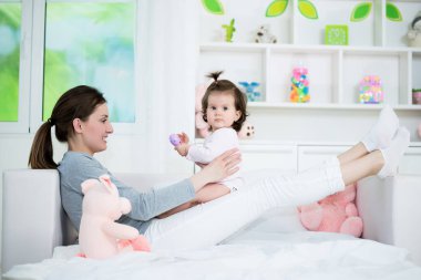 Genç anne yatağa uzanıyor ve mutlu bebeğini kucağında tutuyor. 