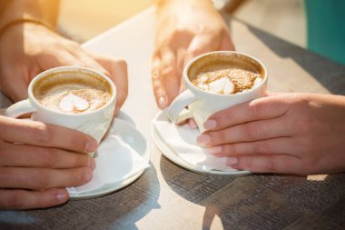 Kadın ve erkeğin elleri açık kafedeki kahve fincanlarının üzerinde..