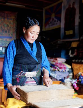 Tibetli yaşlı bir kadın kitap okuyor.