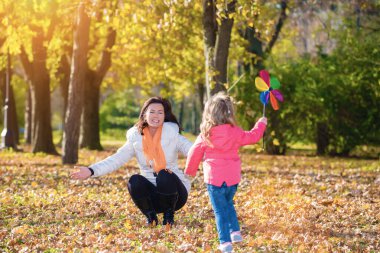 Annesi mutlu koşan kızını sonbahar parkında tutmak için kollarını kaldırdı.
