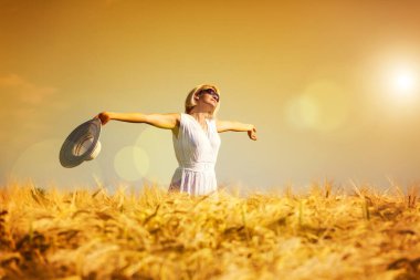 Buğday tarlasında kollarını açmış mutlu, tatmin olmuş genç bir kadın.