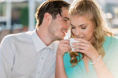 Bir adam kızların kulağına fısıldıyor, kahve içiyor.