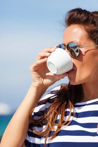 Deniz kenarındaki bir kafede oturup kahve içen güzel bir kadın.