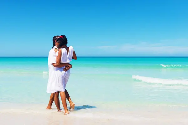 Mutlu, genç çift tropikal sahilde sarılıyor.