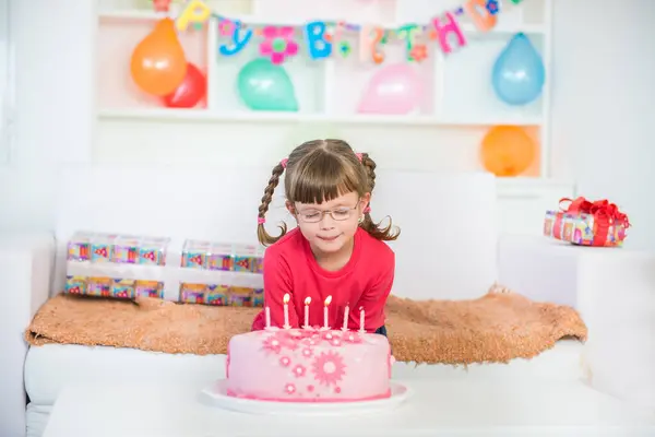 Küçük kız doğum günü partisinde doğum günü pastasının arkasında güzel bir şey diliyor.