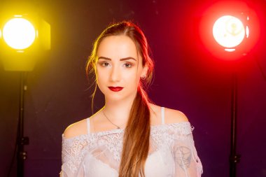 Çekici genç Avrupalı bir kadın stüdyoda poz veriyor, arkadan gelen kırmızı ve sarı renkli dinamik bir ışık karışımı ile banyo yapıyor. Sıcak renkler onun güzelliğini vurgular ve resme sanatsal bir yetenek katar..