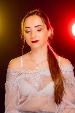 Çekici genç Avrupalı bir kadın stüdyoda poz veriyor, arkadan gelen kırmızı ve sarı renkli dinamik bir ışık karışımı ile banyo yapıyor. Sıcak renkler onun güzelliğini vurgular ve resme sanatsal bir yetenek katar..