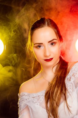 Çekici genç Avrupalı bir kadın stüdyoda poz veriyor, arkadan gelen kırmızı ve sarı renkli dinamik bir ışık karışımı ile banyo yapıyor. Sıcak renkler onun güzelliğini vurgular ve resme sanatsal bir yetenek katar..