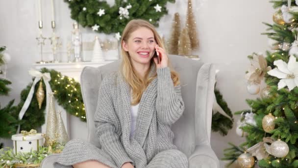 幸せな笑顔で会話を聞いている彼女の携帯電話上のクリスマスの挨拶コールを作る素敵な暖かいセーターの若い女性 — ストック動画