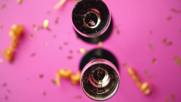 ピンクの背景にコンフェッティとサーペンタインの黄金の装飾が施された輝くシャンパンワインでいっぱいの2つのグラス コピースペース付きのトップビュー 祭りやパーティーのコンセプト — ストック動画